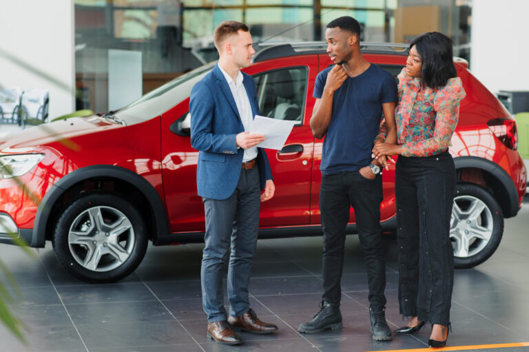 Couple receiving keys from dealership representative, purchasing a new car.